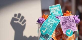 Are Women Still Being Silenced at the Ballot Box? A ballot box overflowing with suffrage flyers, a megaphone, and checkmark confetti.