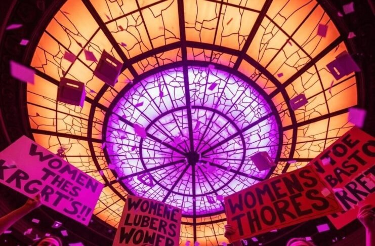 6 Policy Changes That Could Reshape Women’s Rights A blurred, photorealistic protest scene with women's silhouettes, signs, and ballot-box confetti.